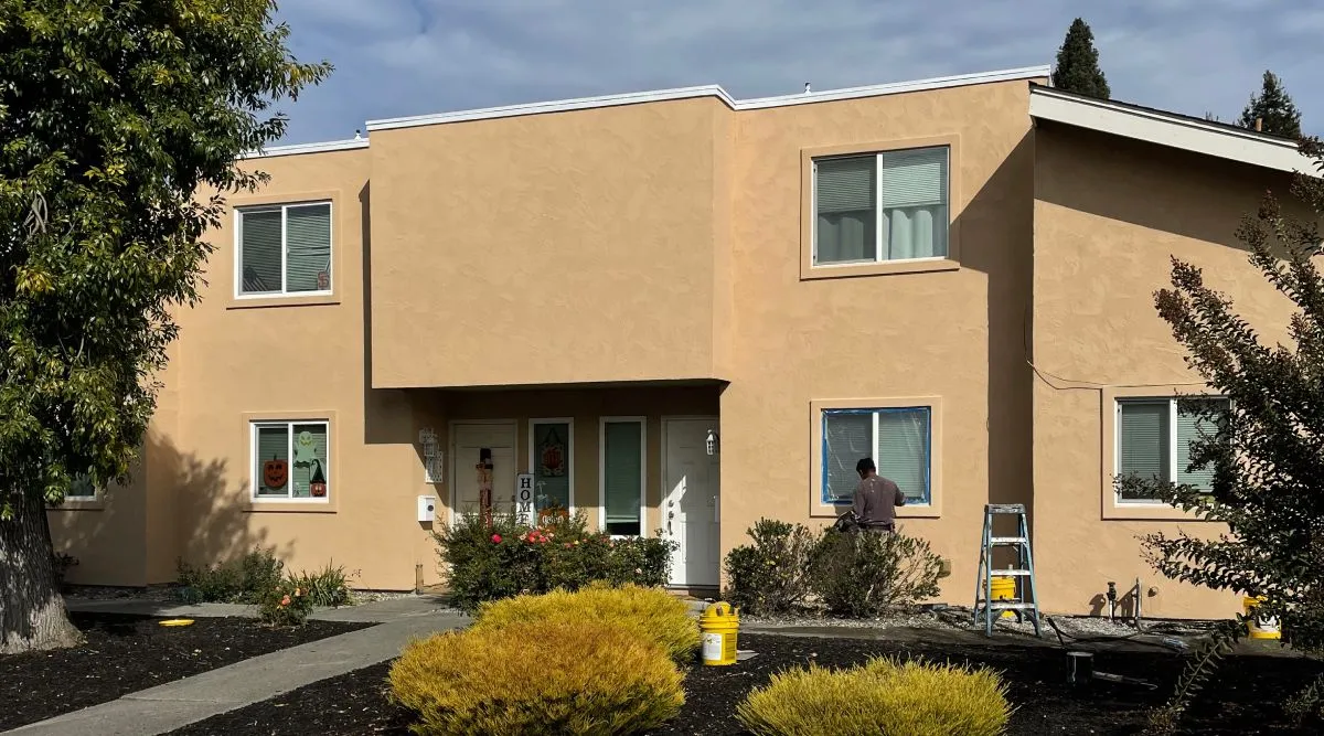 Crew member detailing a window on a townhome with a freshly applied stucco finish coat — stucco repair and restoration