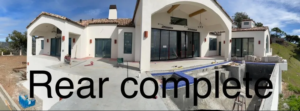 Panorama of the completed rear stucco elevation with arched loggia and pool under construction