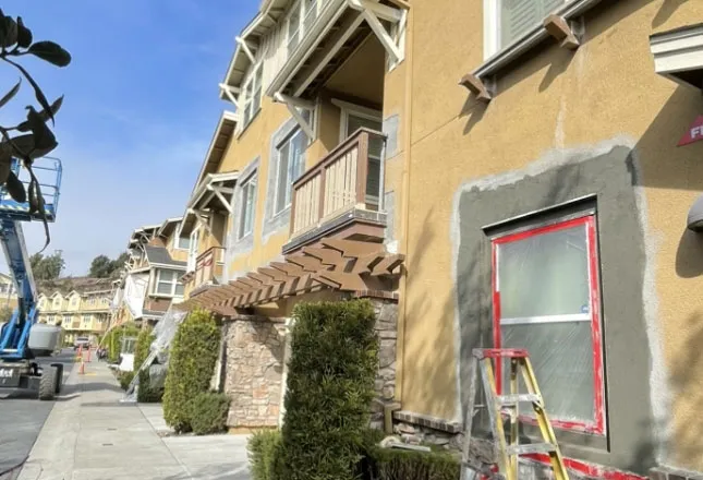 Stucco base coat applied around a window opening on a craftsman townhome, with boom lift on site — window patching and restoration