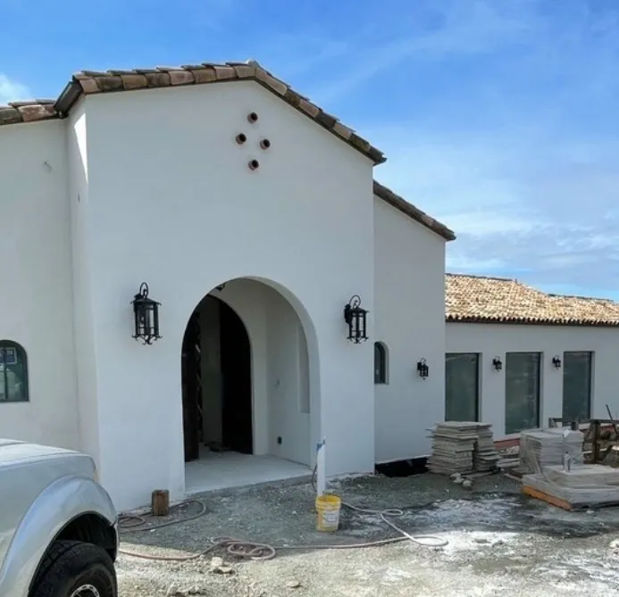 White stucco arched entry with iron lanterns on a Spanish-style new build